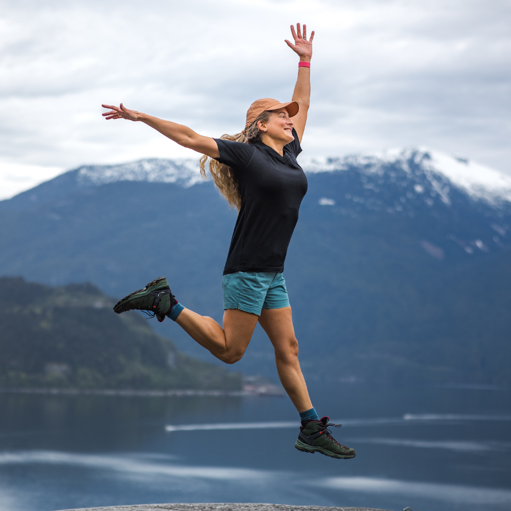 Person jumping in the air with mountains and a lake in the background